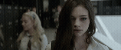 A Girl With Long Dark Hair Looks At The Camera In A Dark Room GIF