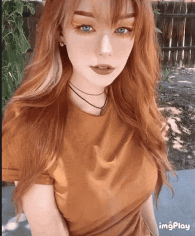 A Girl With Long Red Hair And Blue Eyes Is Wearing A Brown Shirt GIF