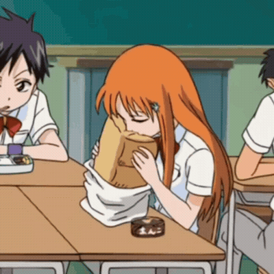A Girl With Orange Hair Is Sitting At A Desk Eating From A Brown Paper Bag GIF