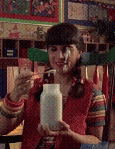 A Girl With Pigtails Is Holding A Jar Of Milk And A Spoon GIF
