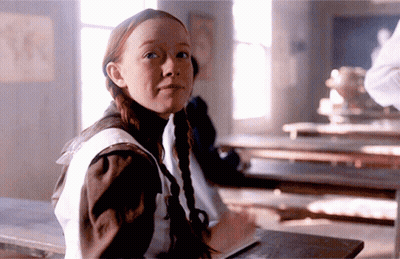 A Girl With Pigtails Is Sitting At A Desk With A Book GIF