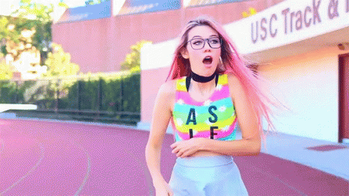 A Girl With Pink Hair Is Running In Front Of The Usc Track And Field Building GIF