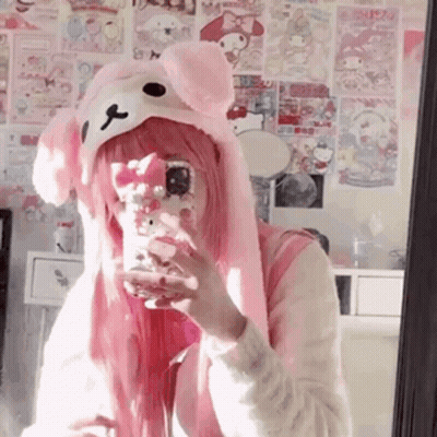 A Girl With Pink Hair Is Taking A Selfie In A Mirror While Wearing A Pink Hat . GIF
