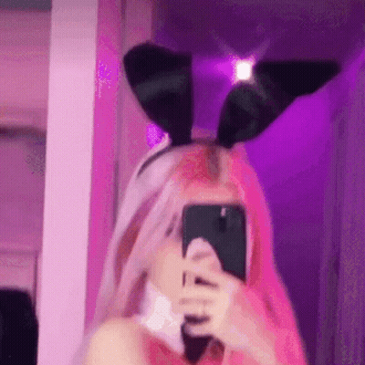 A Girl With Pink Hair Is Taking A Selfie With Her Phone While Wearing Bunny Ears . GIF