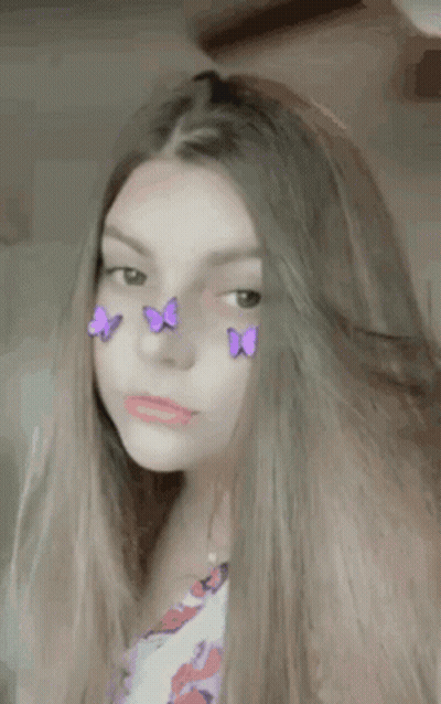 A Girl With Purple Butterflies On Her Face Is Looking At The Camera . GIF
