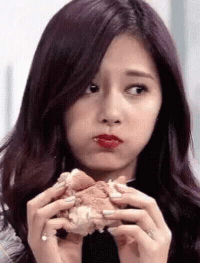 A Girl With Purple Hair Is Eating A Hamburger With Her Mouth Open . GIF