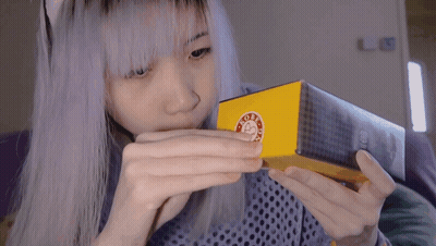 A Girl With Purple Hair Is Holding A Box With A Sticker On It That Says ' Good Day ' GIF
