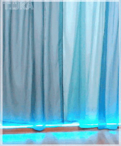 A Girl With Red Hair And Glasses Stands In Front Of A Blue Curtain With The Word Tdka Written On It GIF