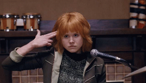 A Girl With Red Hair Is Sitting In Front Of A Microphone Making A Salute Gesture GIF