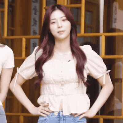 A Girl With Red Hair Is Standing With Her Hands On Her Hips In Front Of A Window GIF