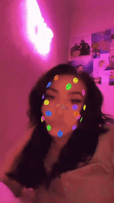 A Girl With Smiley Faces On Her Face And A Pink Light In The Background GIF