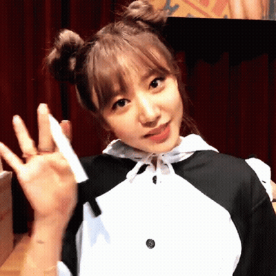 A Girl With Two Buns On Her Hair Is Waving Her Hand GIF