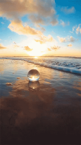 A Glass Ball Sits On The Beach Near The Water GIF