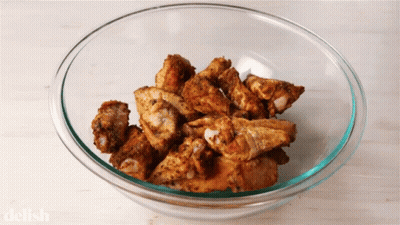 A Glass Bowl Filled With Fried Chicken Wings With The Word Delish On The Bottom GIF