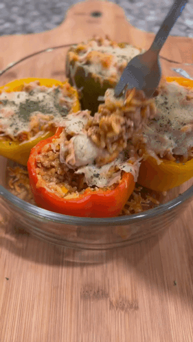 A Glass Bowl Of Stuffed Peppers With Rice And Cheese GIF