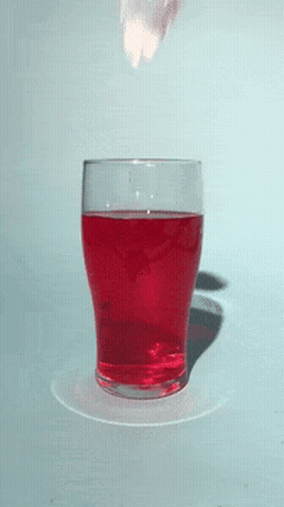 A Glass Filled With Red Liquid With A Strawberry Splashing Out Of It GIF