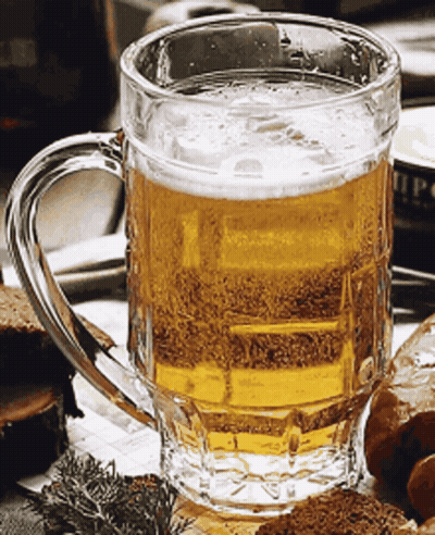 A Glass Mug Filled With Beer Sits On A Table Next To Some Bread GIF