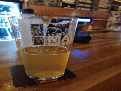 A Glass Of Beer Sits On A Coaster That Says Miami Brew GIF