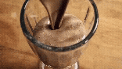 A Glass Of Chocolate Milkshake Is Being Poured Into A Glass . GIF