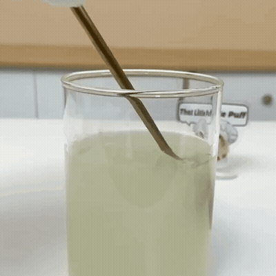 A Glass Of Liquid With A Spoon In It And A Sticker That Says That Little Puff GIF
