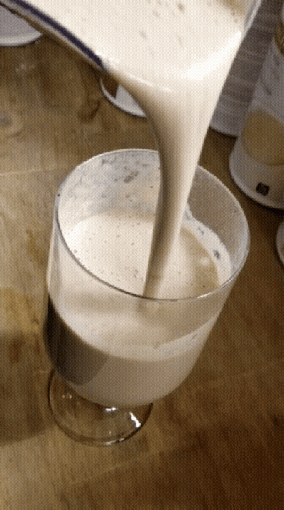A Glass Of Milk Is Being Poured Into A Glass On A Wooden Table GIF