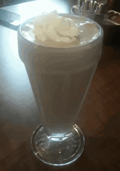 A Glass Of Milkshake With Whipped Cream On Top On A Table GIF