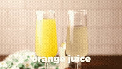 A Glass Of Orange Juice Is Being Poured Into A Glass Of Wine GIF