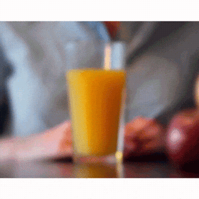 A Glass Of Orange Juice Is On A Table Next To Apples GIF