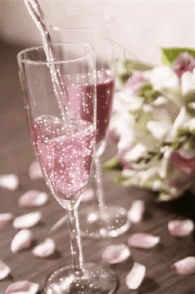 A Glass Of Pink Champagne Is Being Poured Into A Glass On A Table . GIF