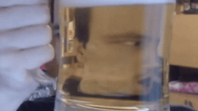 A Glass Of Water Is Sitting On A Table In Front Of A Window GIF