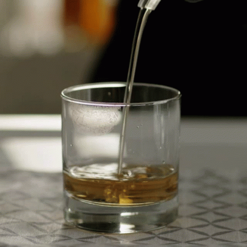 A Glass Of Whiskey Is Being Poured Into A Glass On A Table GIF