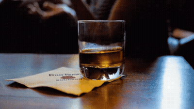 A Glass Of Whiskey Sits On A Napkin With Four Roses Written On It GIF