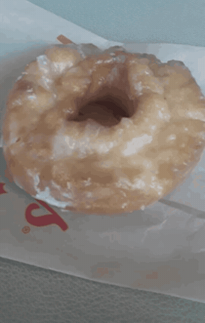 A Glazed Donut Is Sitting On A Piece Of Paper That Says ' S ' On It GIF