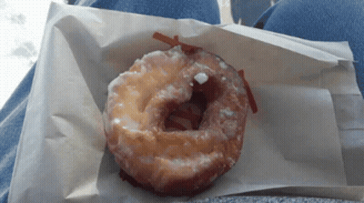A Glazed Donut Is Sitting On A Piece Of Paper GIF