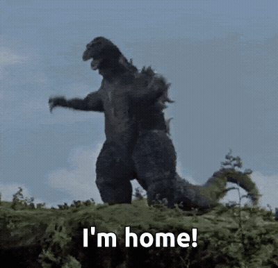 A Godzilla Is Standing On Top Of A Pile Of Grass And Says I 'M Home . GIF