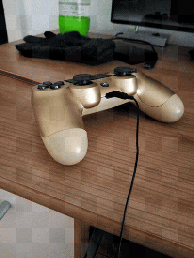 A Gold Video Game Controller Is Sitting On A Wooden Desk GIF