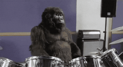 A Gorilla Is Playing Drums In A Room In Front Of A Purple Wall . GIF