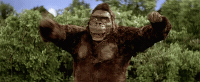 A Gorilla With Its Arms Outstretched Is Standing In Front Of Trees GIF