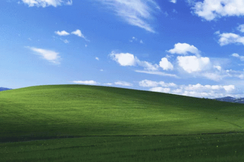 A Grassy Hill With A Blue Sky And White Clouds Behind It GIF