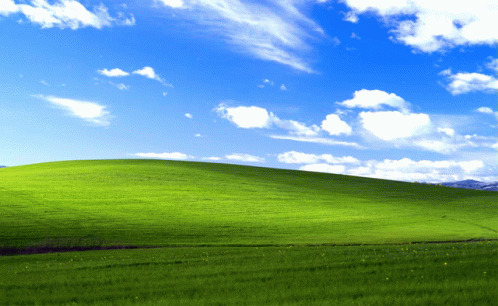 A Grassy Hill With A Blue Sky And White Clouds Behind It GIF