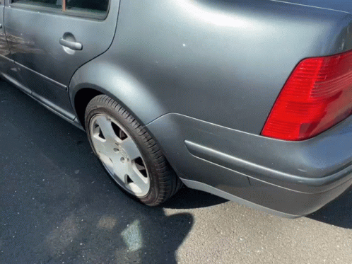 A Gray Car With A Red Tail Light Is Parked On The Side Of The Road GIF