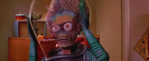 A Green Alien Is Standing In A Room With A Lamp And A Clock . GIF