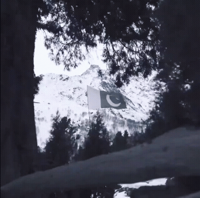 A Green And White Flag Is Flying In Front Of A Snow Covered Mountain GIF