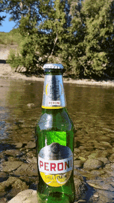 A Green Bottle Of Peroni Sits On A Rock Near A River GIF