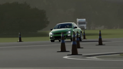 A Green Car Is Driving Past A Traffic Cone On A Road GIF