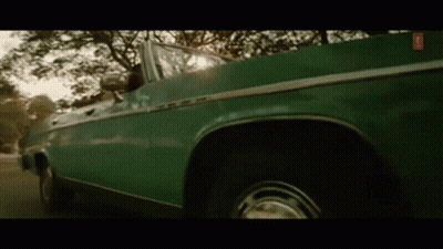 A Green Convertible Car Is Driving Down A Street . GIF