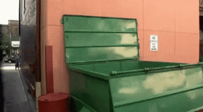 A Green Dumpster Is Sitting On The Side Of A Building GIF