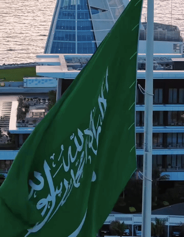 A Green Flag With Arabic Writing On It Flies In Front Of A Building GIF