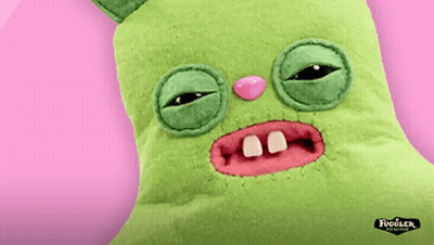 A Green Fugler Stuffed Animal With A Pink Nose And Teeth On A Pink Background GIF