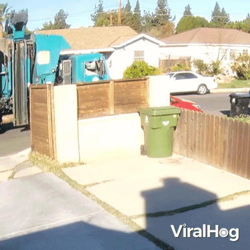 A Green Garbage Can Sits In Front Of A Wooden Fence With A Viralhog Logo On The Bottom GIF
